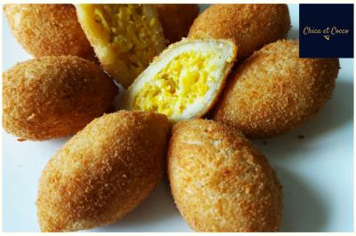 Assiette garnie de beignets dorés en forme de demi-lune, présentée sur une table avec une coupe en arrière-plan.