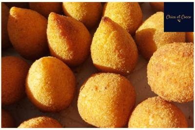 Assiette garnie de beignets dorés en forme de demi-lune, présentée sur une table avec une coupe en arrière-plan.