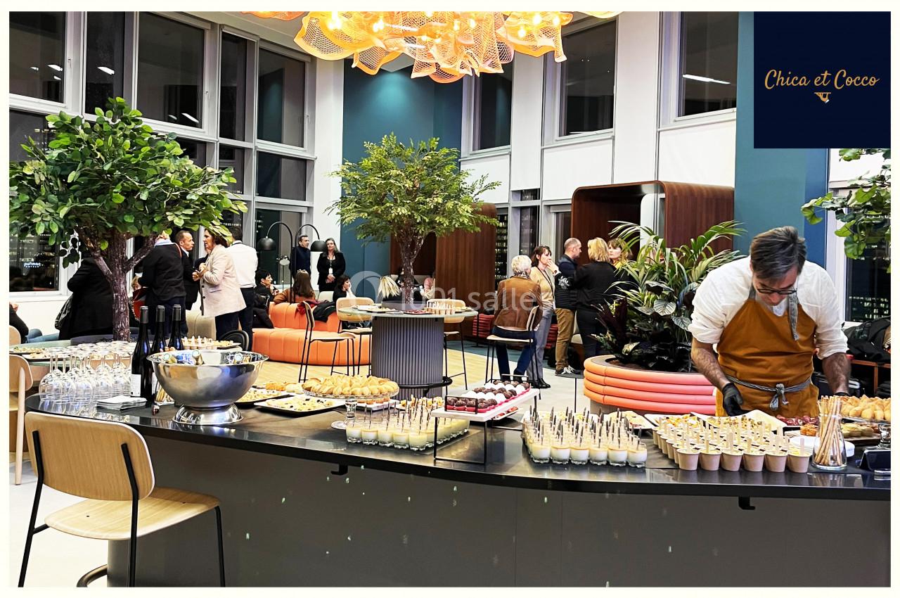 Buffet élégant avec verrines et amuse-bouches dans un espace moderne, des invités discutent en arrière-plan.