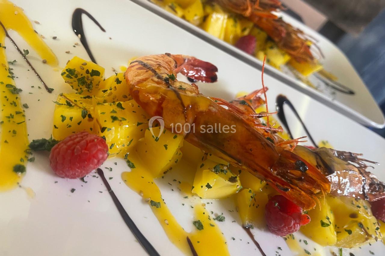 Assiette gastronomique avec gambas grillées, cubes de mangue, framboises et filet de sauce balsamique décorative.