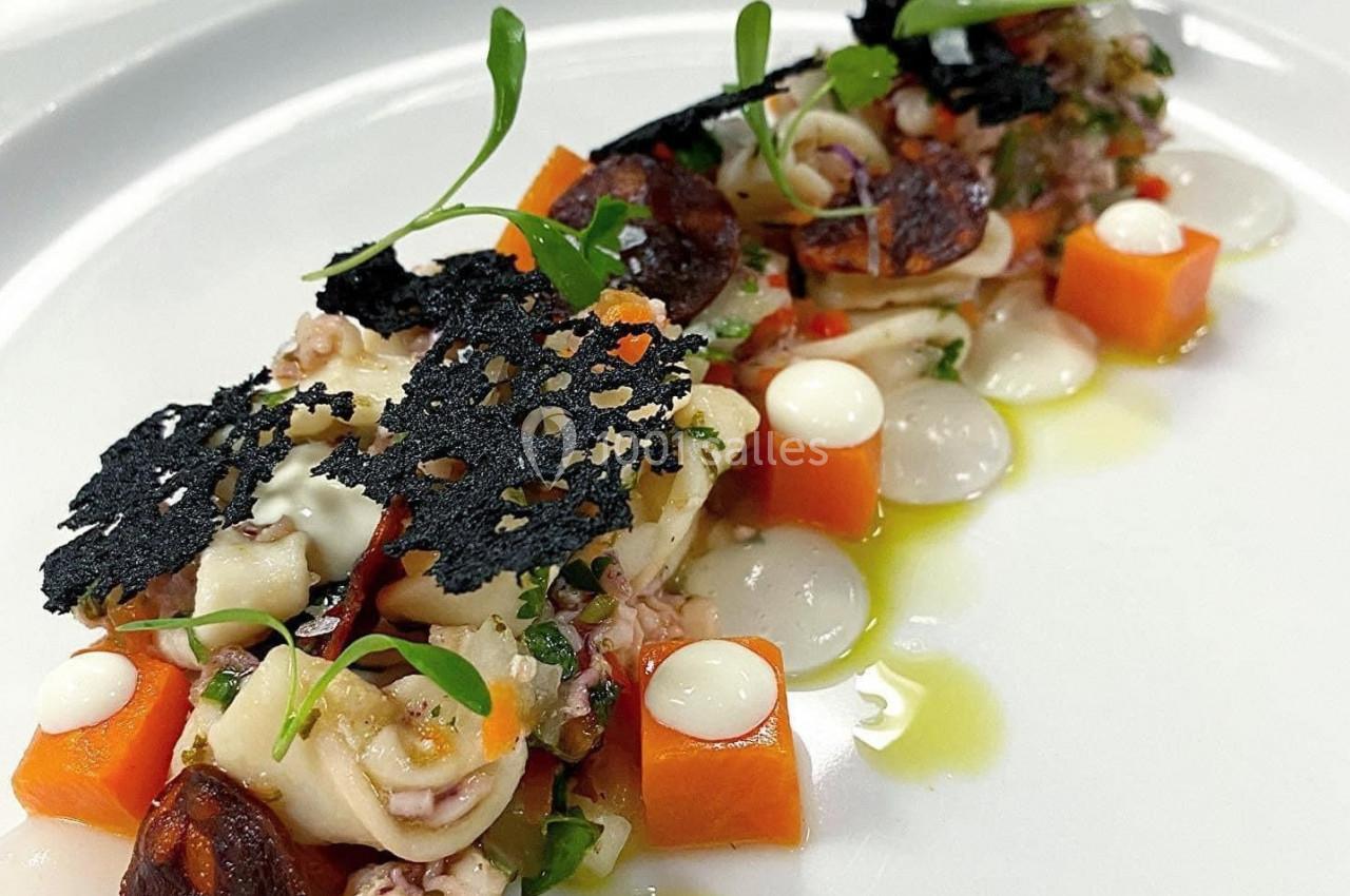 Assiette gastronomique composée de fruits de mer, cubes de légumes, émulsions blanches et tuiles noires décoratives.