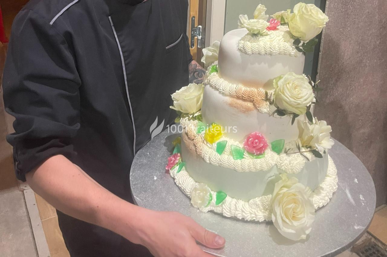 Un pâtissier tenant un gâteau de mariage à trois étages décoré de fleurs blanches et roses.