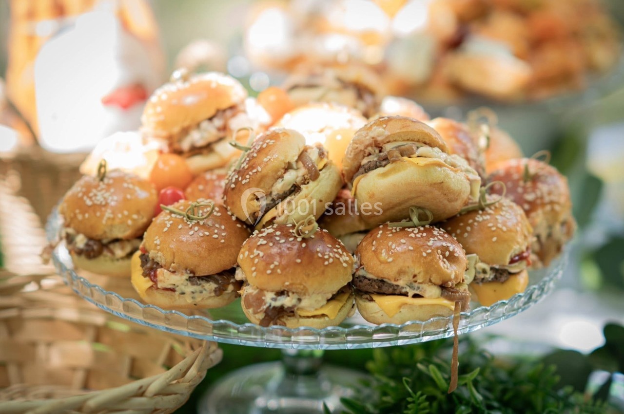 Plateau de mini-burgers garnis, disposés sur un présentoir en verre, entouré d'éléments décoratifs.