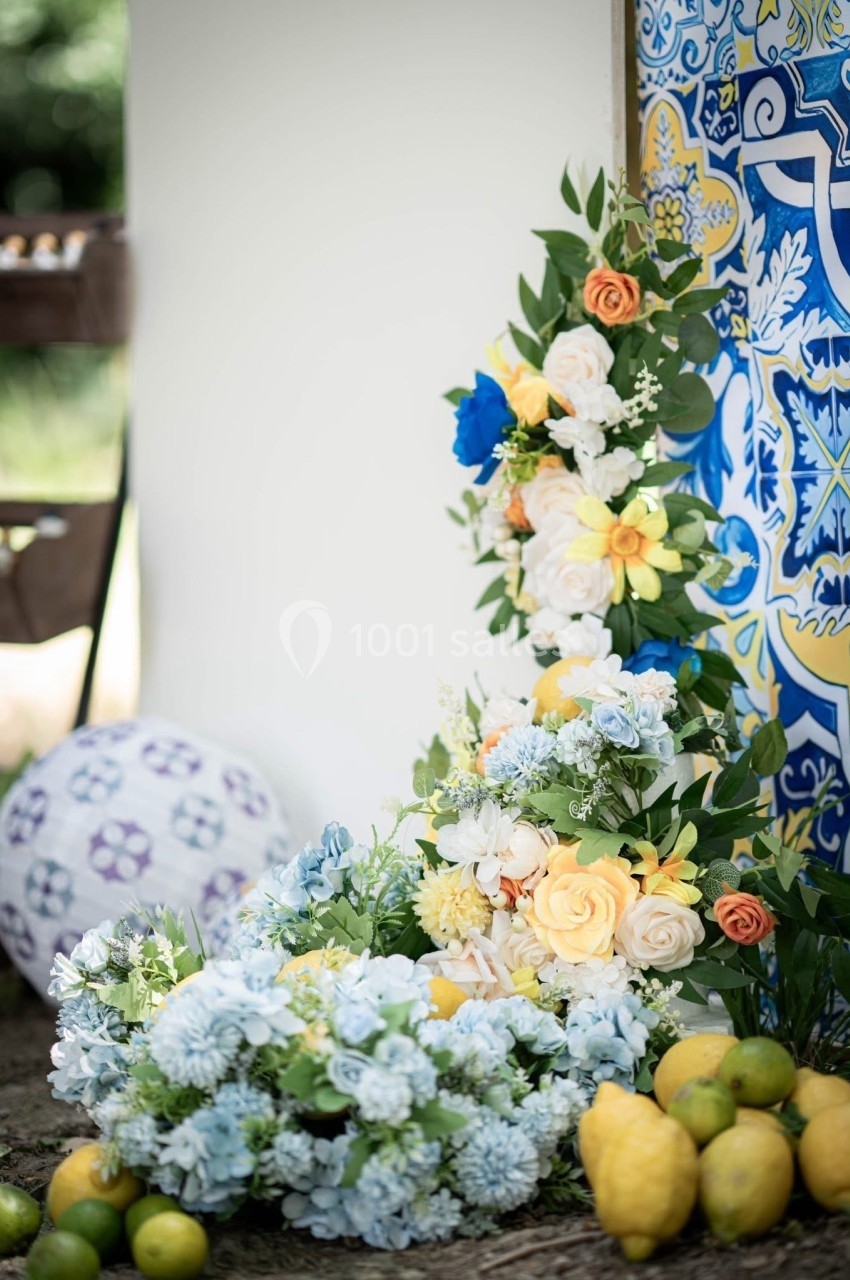 Arrangement floral coloré avec des roses et des fleurs bleues, entouré de citrons et d'un décor en carreaux bleus.