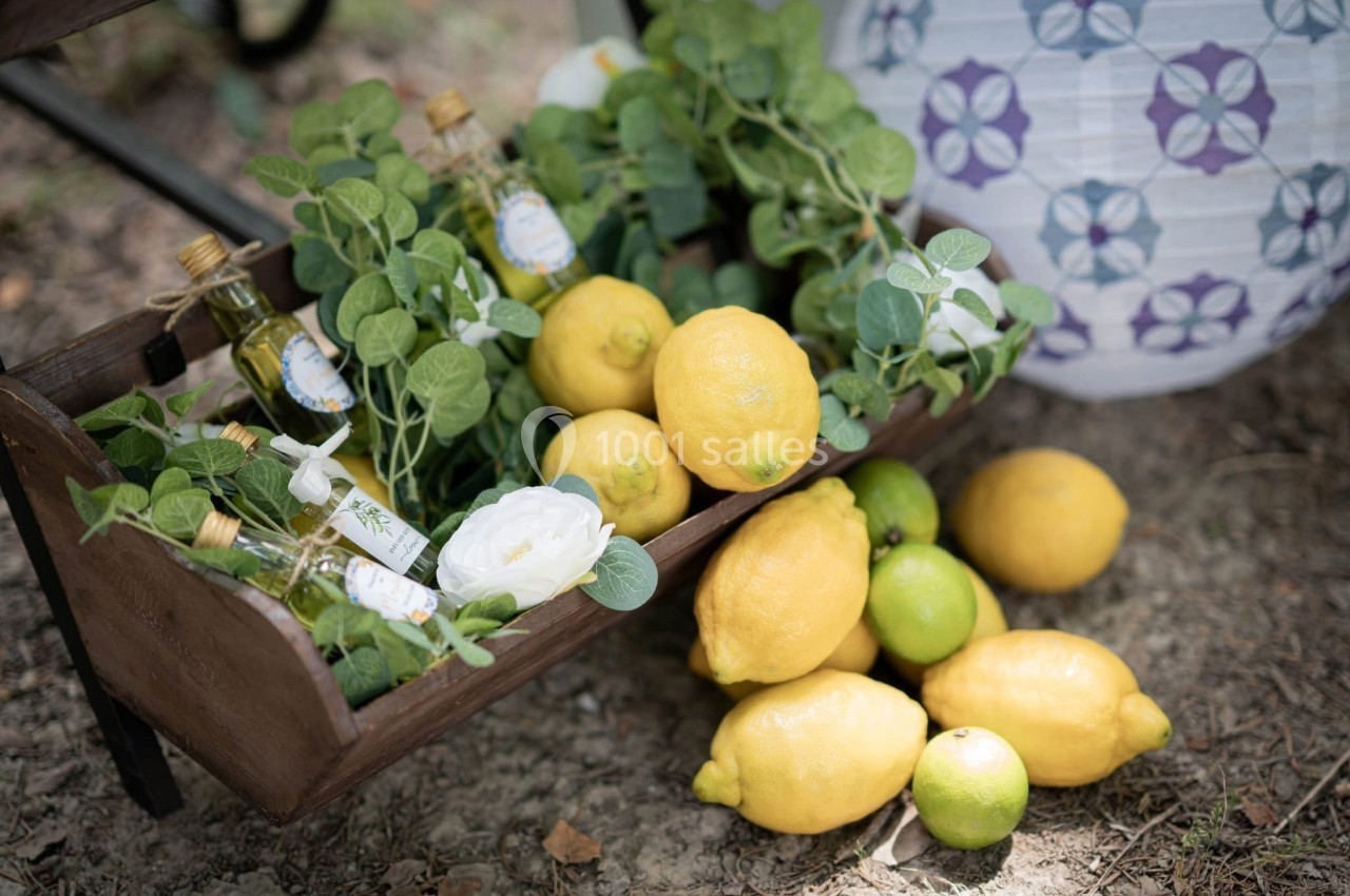 Cagette en bois contenant des citrons, des citrons verts, des bouteilles d'huile et des feuillages, posée sur un sol…