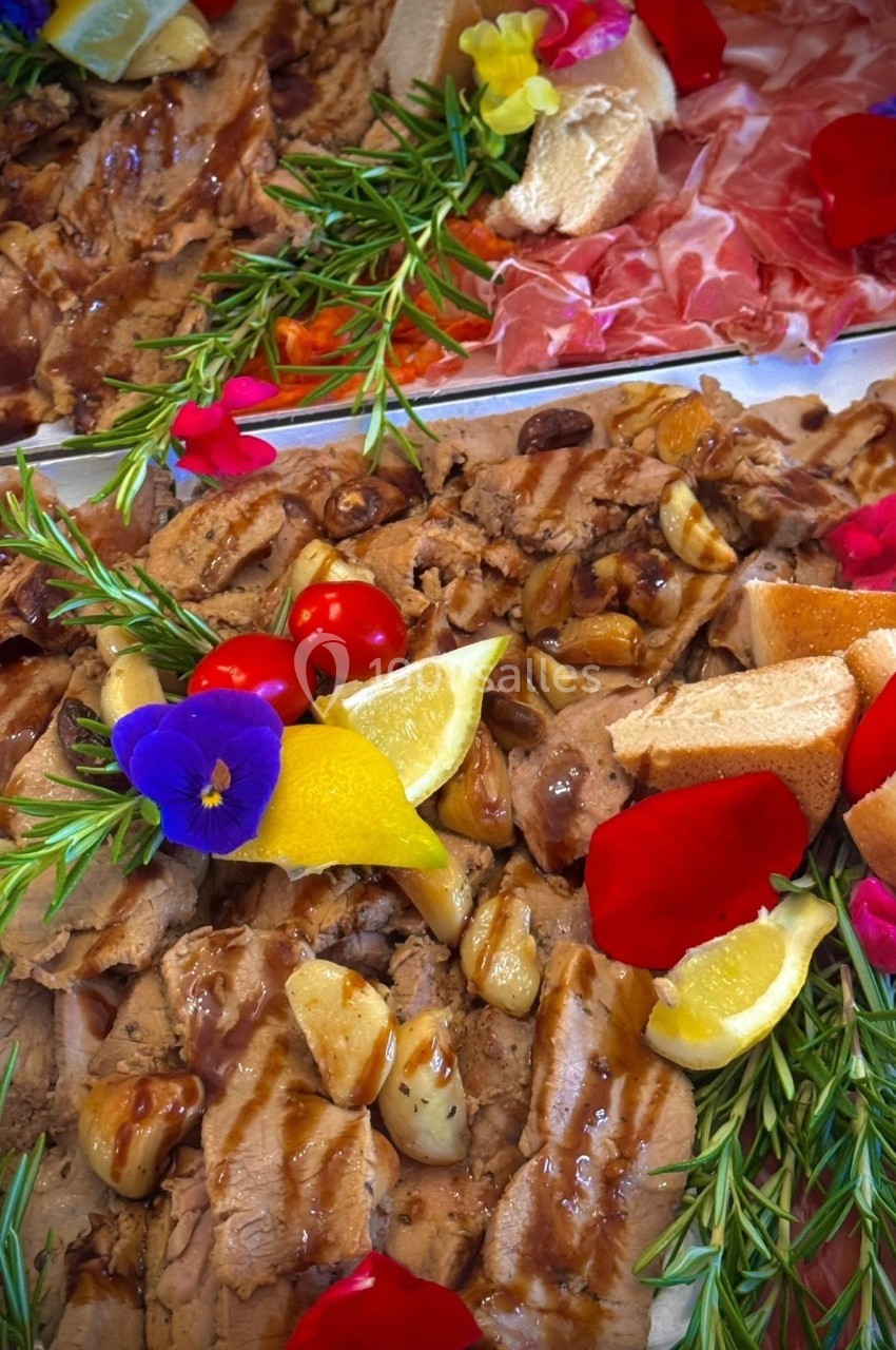 Plateau garni de viandes, herbes fraîches, tomates cerises, tranches de citron, ail rôti et fleurs comestibles.
