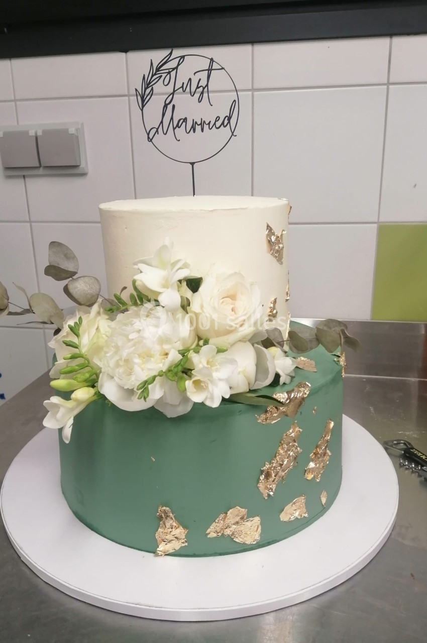 Gâteau à deux étages décoré de fleurs blanches, feuilles d'eucalyptus et éclats dorés, surmonté d'un cake topper.