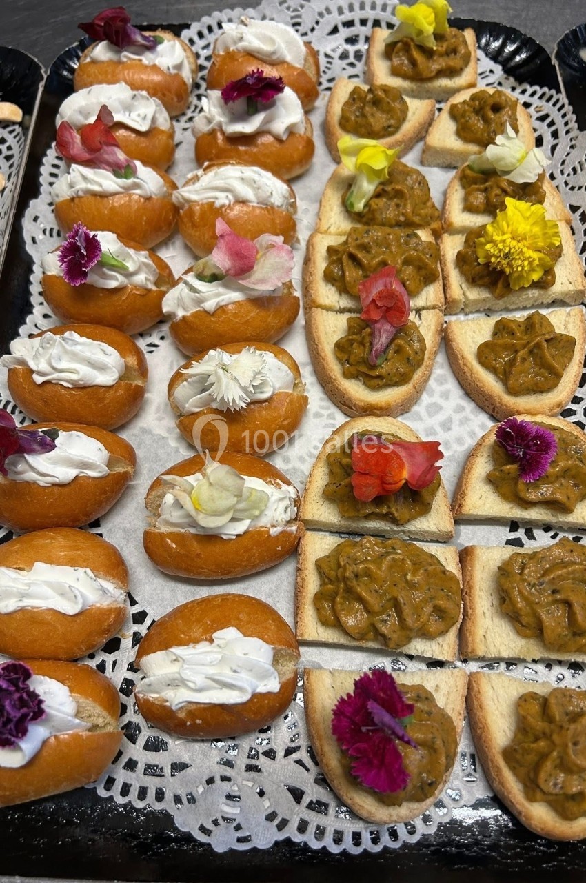 Plateau de bouchées apéritives variées avec fleurs comestibles, crème et tartinades sur pain et pâte.