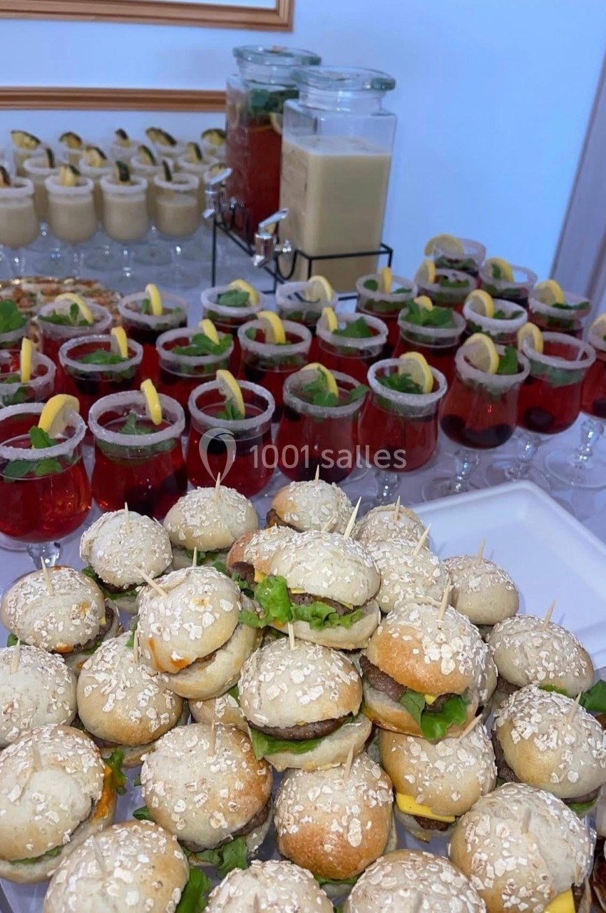 Plateau de mini-burgers garnis devant des verrines de cocktails colorés et des boissons en carafes.