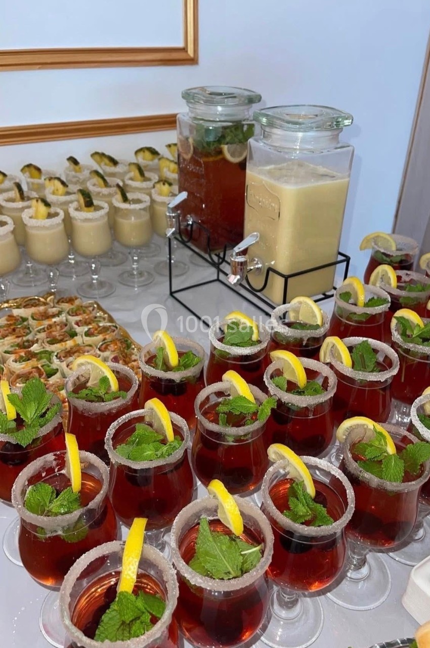 Buffet avec cocktails rouges garnis de citron et menthe, verrines, roulés apéritifs et boissons en distributeurs.