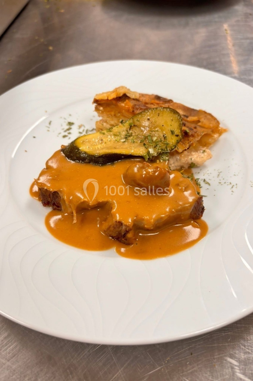 Assiette contenant une viande nappée de sauce brune, accompagnée de gratin et d'une tranche de courgette grillée.