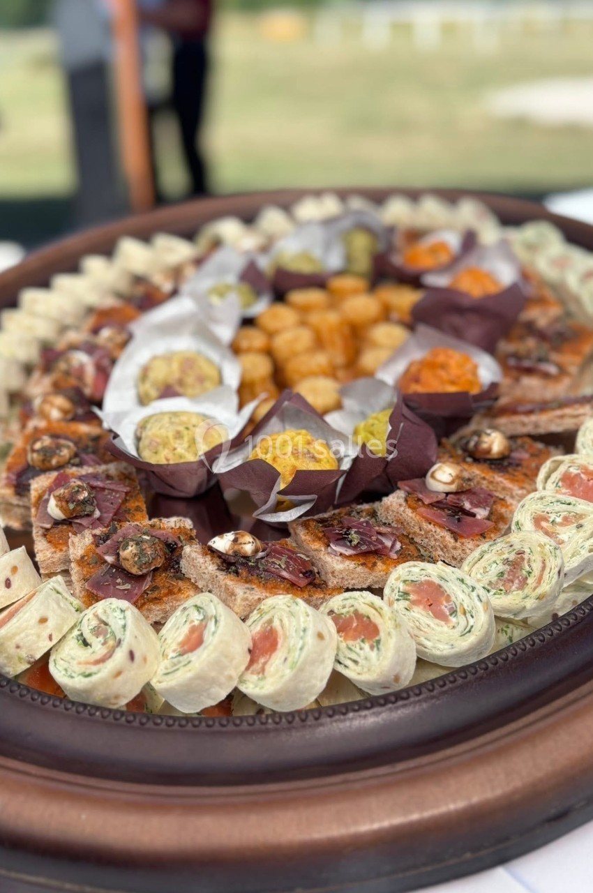Plateau de bouchées apéritives variées comprenant wraps, toasts garnis et boulettes, présenté sur un plat en bois.
