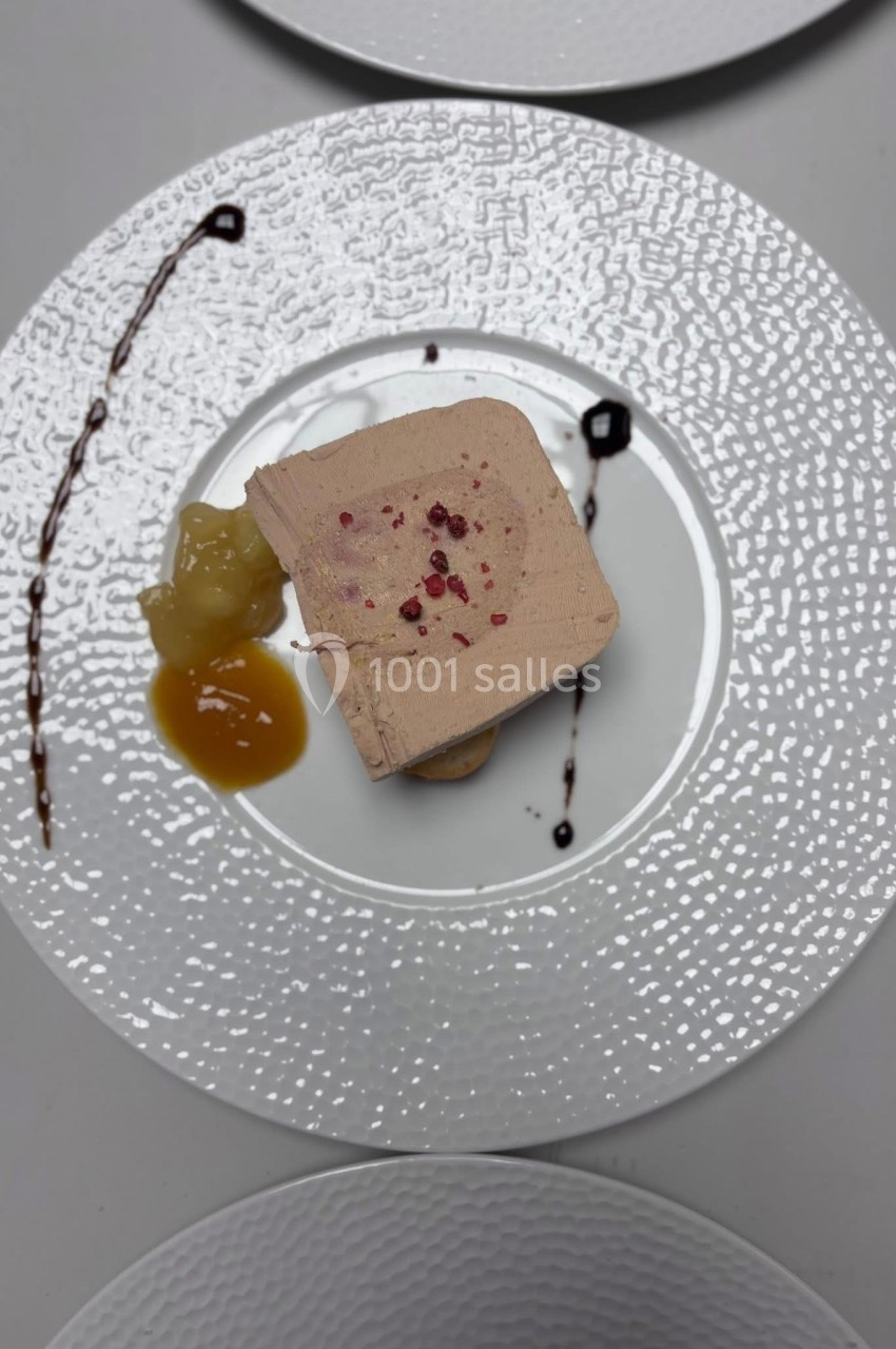 Tranche de foie gras servie avec chutney et décorée de traits de sauce sur une assiette texturée blanche.