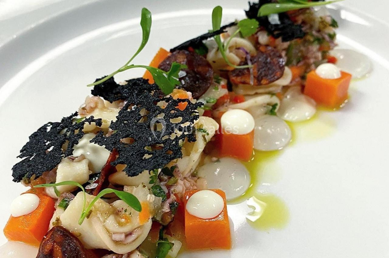 Assiette gastronomique avec présentation soignée de fruits de mer, légumes colorés, tuiles noires et sauces décoratives.