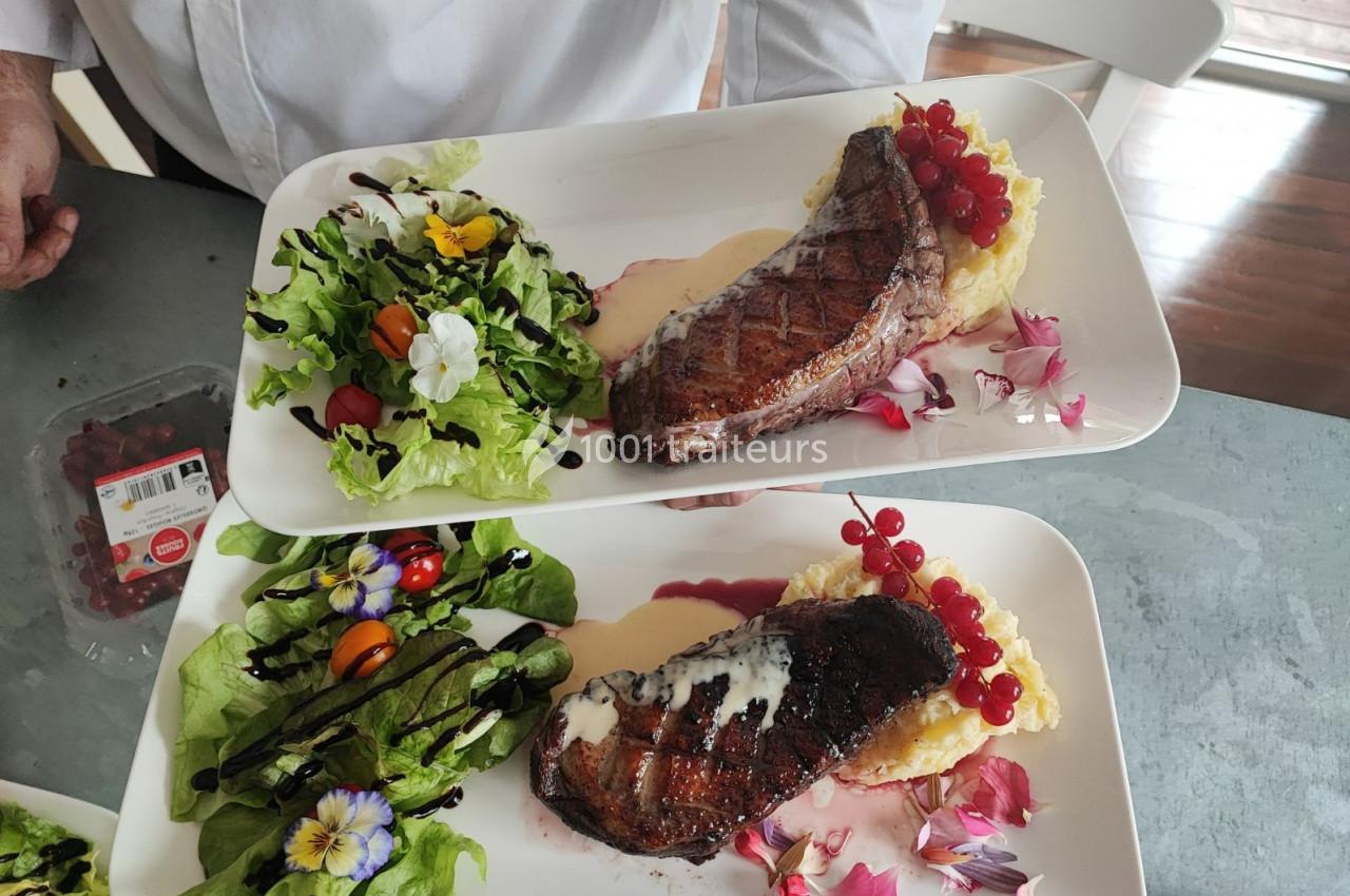 Assiettes composées de steaks grillés, purée, groseilles rouges, salade verte garnie de fleurs comestibles et sauce.