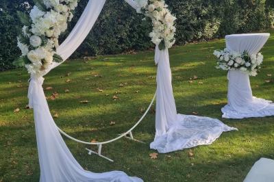 Table décorée avec des flûtes en verre, un bouquet de fleurs blanches, une bougie et des fauteuils ornés en arrière-plan.