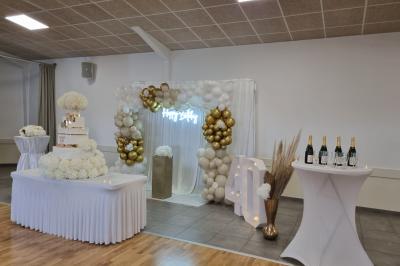 Table décorée avec des flûtes en verre, un bouquet de fleurs blanches, une bougie et des fauteuils ornés en arrière-plan.