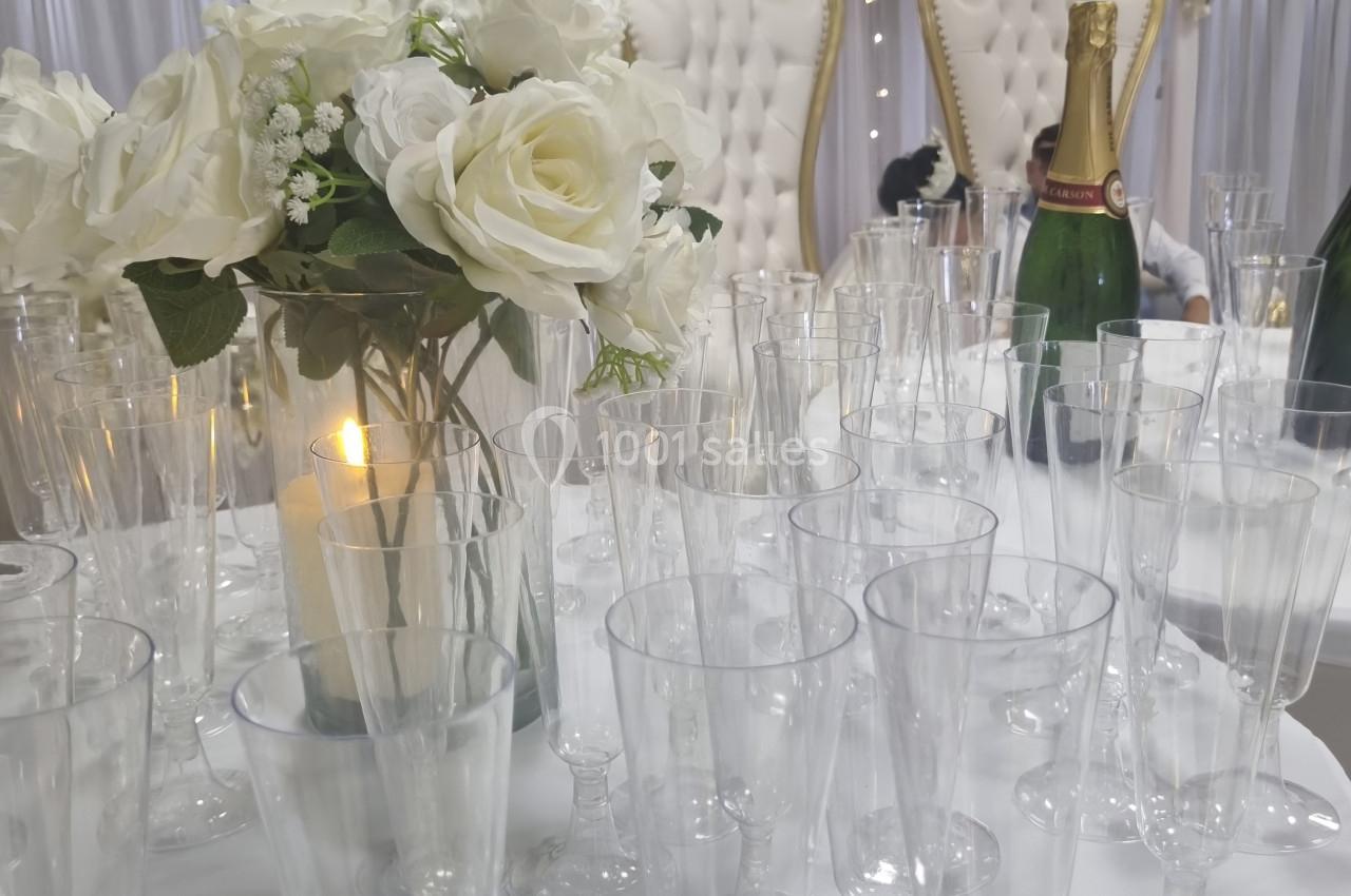 Table décorée avec des flûtes en verre, un bouquet de fleurs blanches, une bougie et des fauteuils ornés en arrière-plan.
