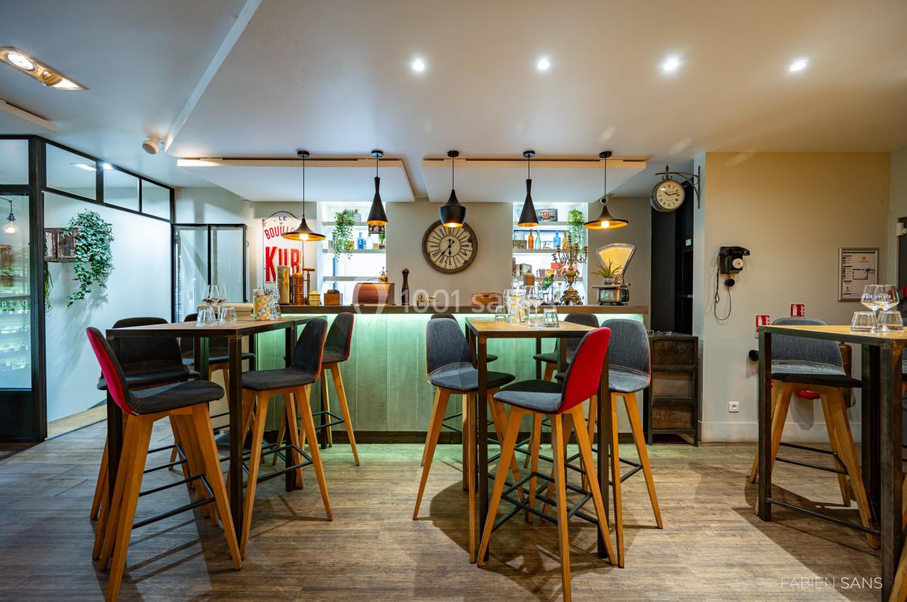 Salle de restaurant moderne avec tables hautes, chaises colorées et comptoir éclairé en arrière-plan.