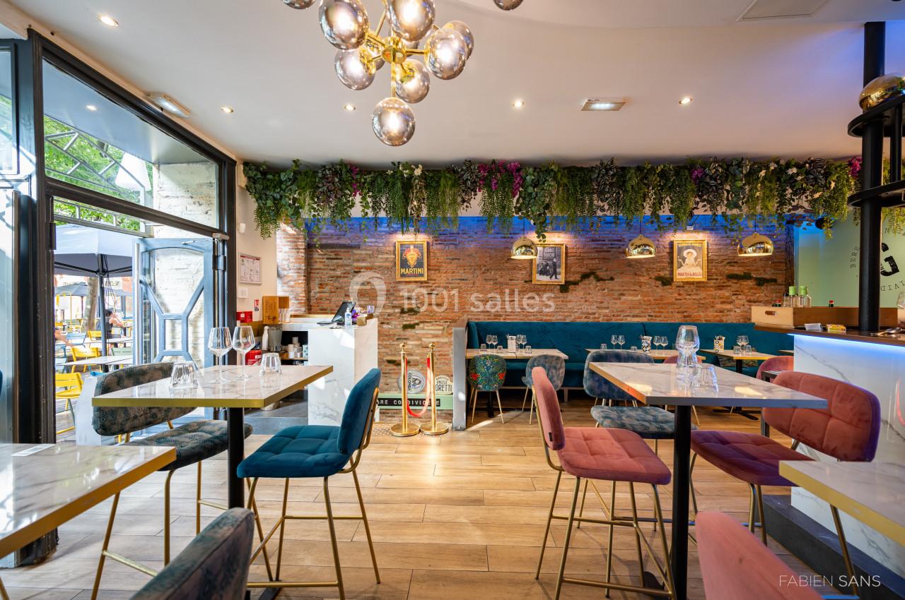 Intérieur d'un restaurant moderne avec tables, chaises colorées, mur en briques, plantes suspendues et éclairage chaleureux.