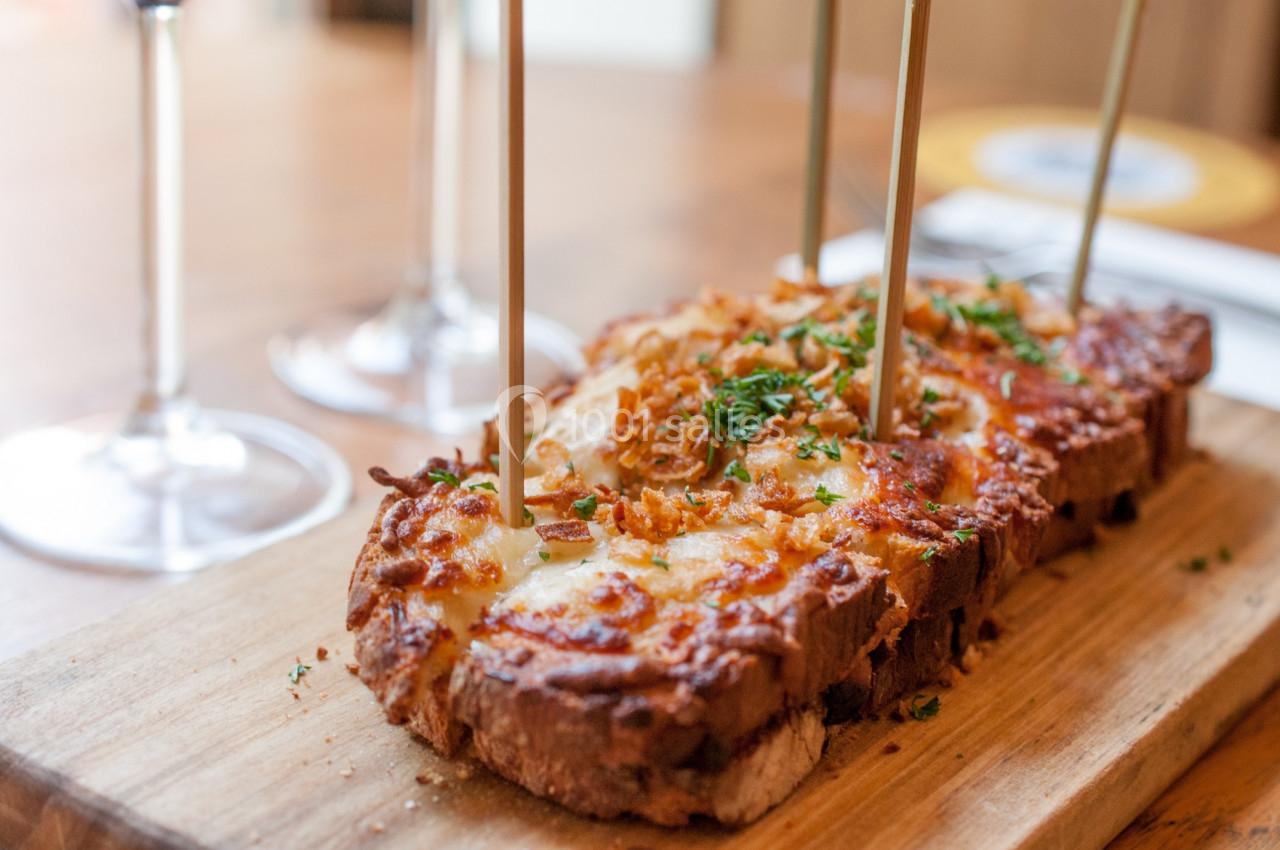 Tranche de pain gratinée au fromage et garnie d'herbes fraîches, servie sur une planche en bois.