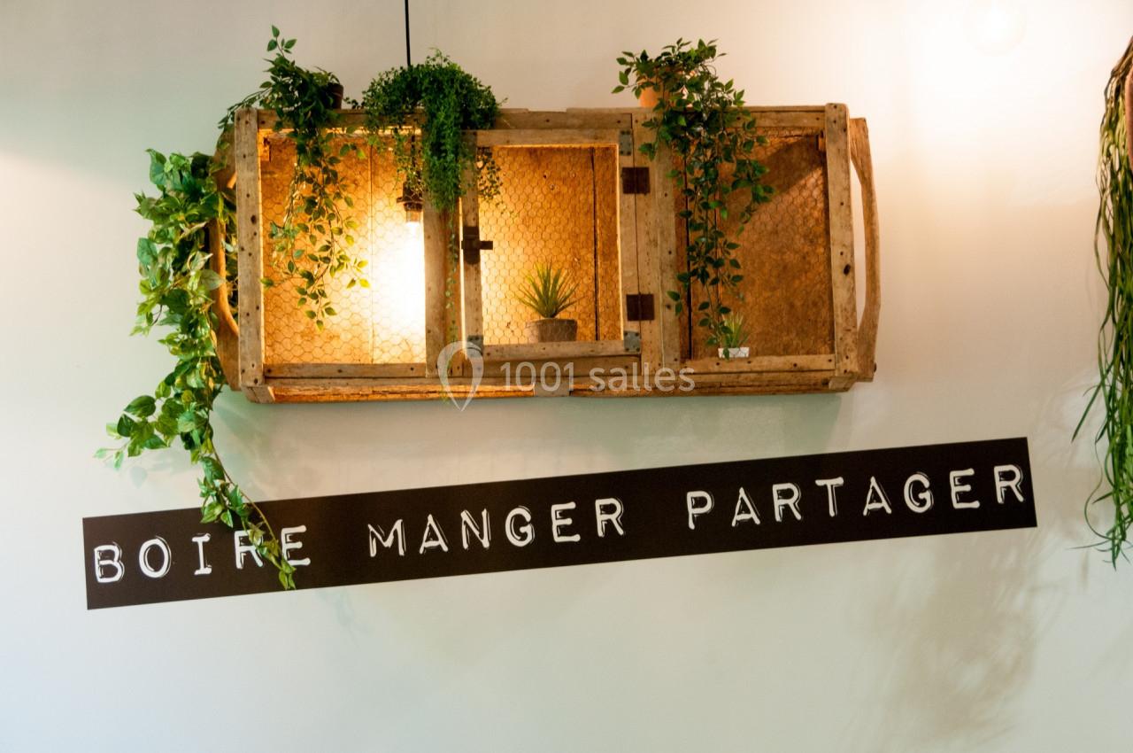 Étagère murale en bois avec plantes suspendues et éclairage, accompagnée de l'inscription ’Boire Manger Partager’.
