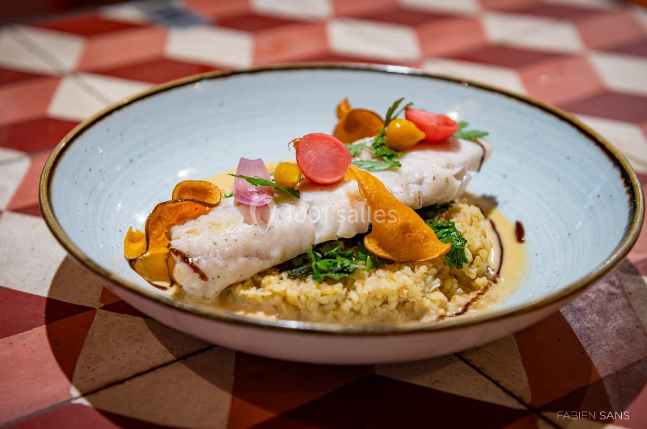 Filet de poisson blanc sur lit de boulgour, décoré de légumes colorés et chips de patate douce, dans une assiette bleue.