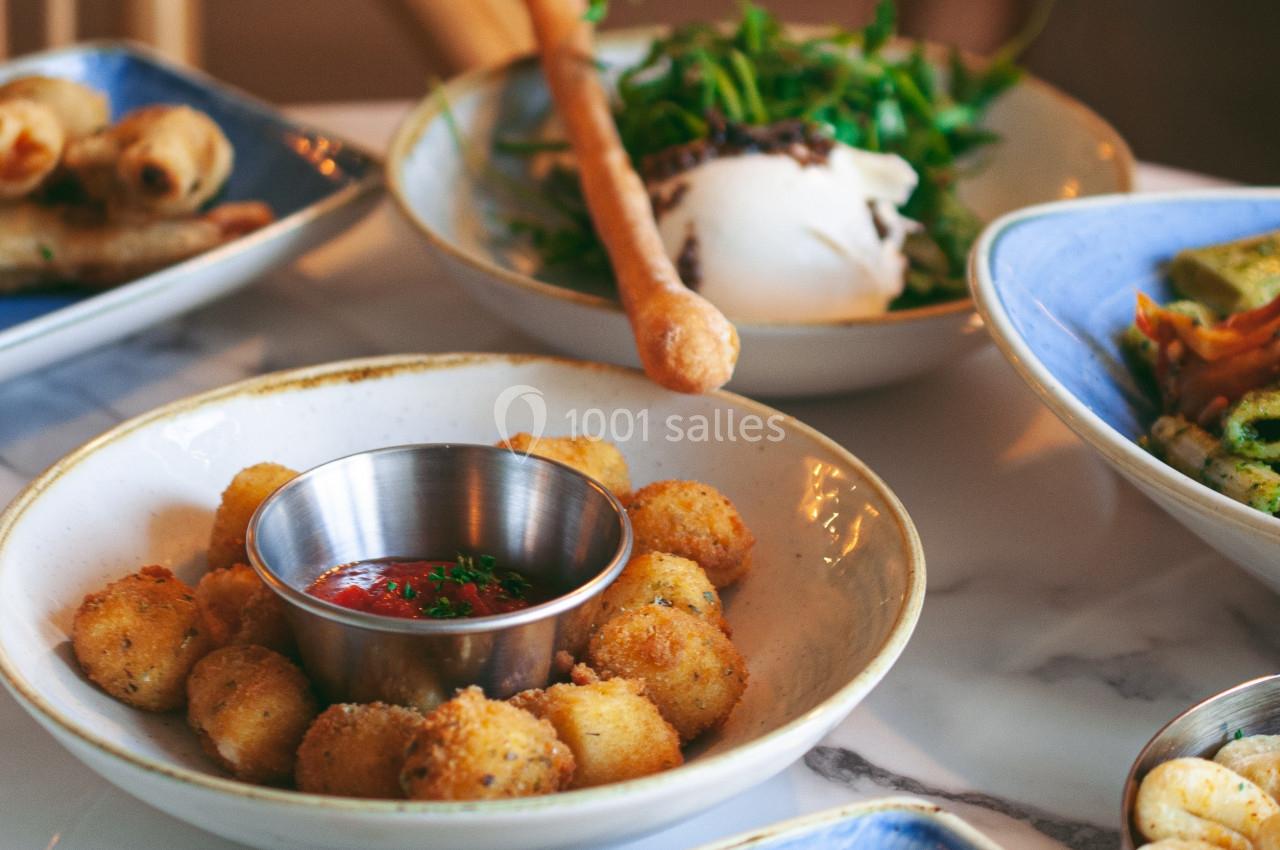 Assiette de boulettes dorées accompagnées d'une sauce rouge, entourée de plats variés sur une table en marbre.