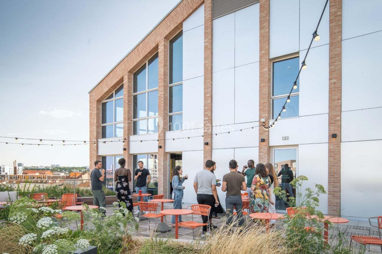 Location salle Ivry-sur-Seine (Val-de-Marne) - Walter Ivry #13 Groupe de personnes discutant sur une terrasse aménagée avec des tables, des chaises et des guirlandes lumineuses.