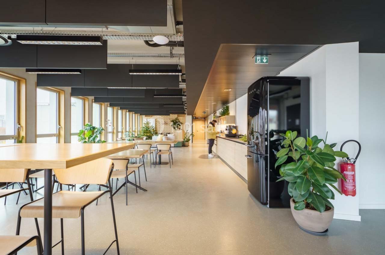 Location salle Ivry-sur-Seine (Val-de-Marne) - Walter Ivry #14 Espace de coworking lumineux avec tables, chaises, plantes, cuisine équipée et grandes fenêtres.