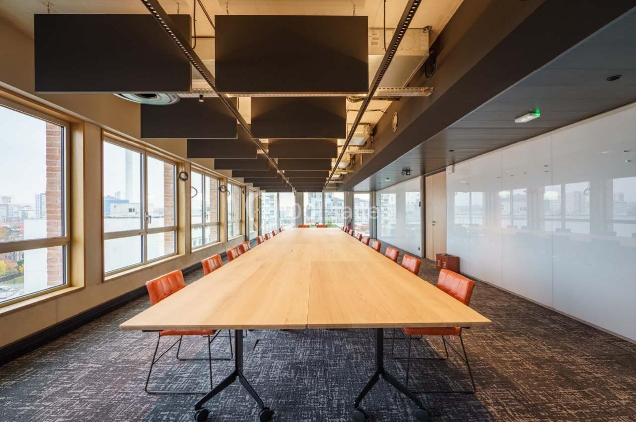 Location salle Ivry-sur-Seine (Val-de-Marne) - Walter Ivry #7 Salle de réunion lumineuse avec une grande table en bois, chaises orange et baies vitrées donnant sur la ville.