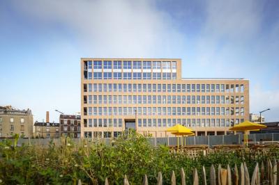 Miniature Location salle Ivry-sur-Seine (Val-de-Marne) - Walter Ivry #16 Bâtiment moderne en briques avec de grandes fenêtres, entouré de végétation et de parasols jaunes au premier plan.