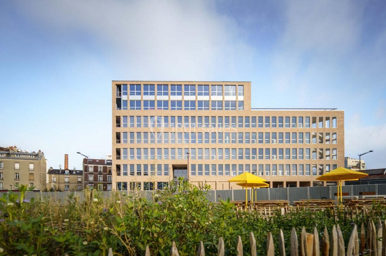 Location salle Ivry-sur-Seine (Val-de-Marne) - Walter Ivry #16 Bâtiment moderne en briques avec de grandes fenêtres, entouré de végétation et de parasols jaunes au premier plan.