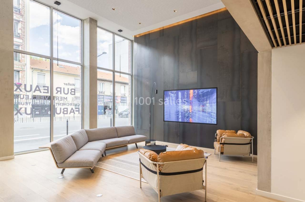 Location salle Ivry-sur-Seine (Val-de-Marne) - Walter Ivry #10 Salon moderne avec canapés et fauteuils en cuir, grande baie vitrée laissant entrer la lumière naturelle, écran mural allumé.