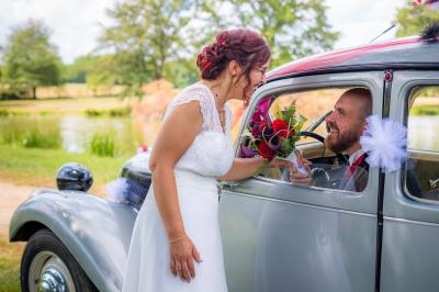 Femme en robe de mariée blanche tenant un bouquet de fleurs blanches et décorations bleues, en extérieur sur pelouse.