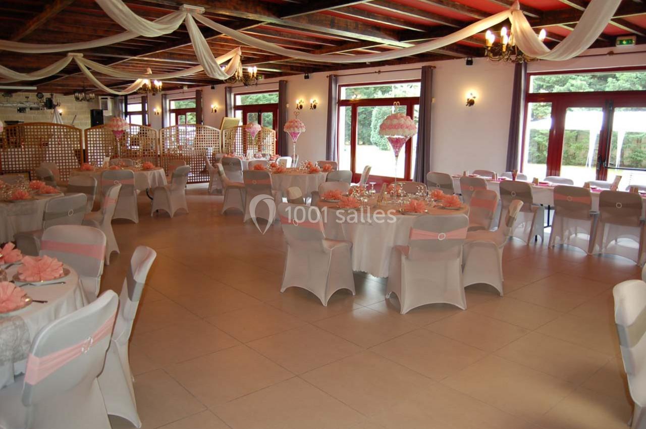 Salle de réception décorée avec des nappes blanches, des rubans roses et des centres de table fleuris.