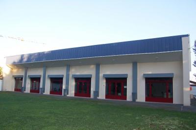 Cuisine professionnelle avec carrelage beige, plans de travail en inox, évier, réfrigérateur et éclairage fluorescent.