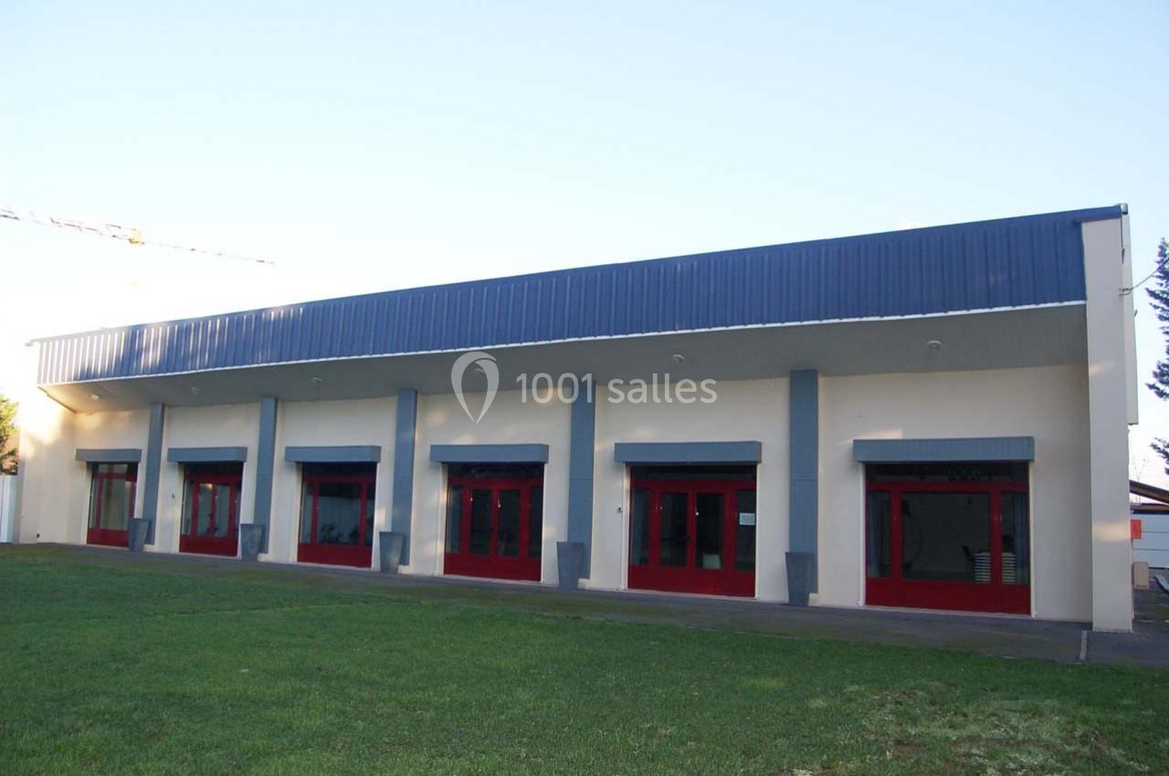 Bâtiment avec façade blanche, toit bleu et plusieurs portes vitrées rouges donnant sur une pelouse verte.