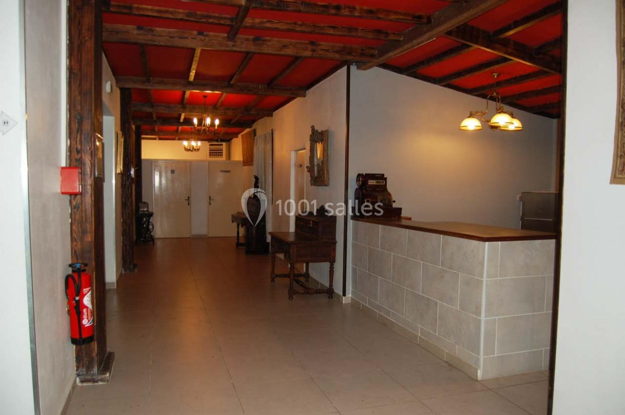 Couloir intérieur avec plafond en bois, murs blancs, comptoir à droite et porte au fond.