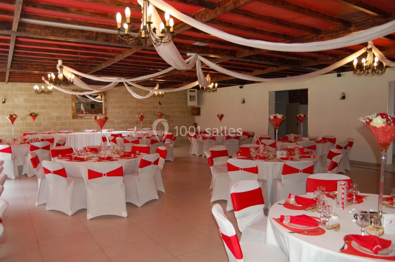 Salle de réception décorée avec des nappes blanches et rouges, des chaises assorties et des centres de table fleuris.