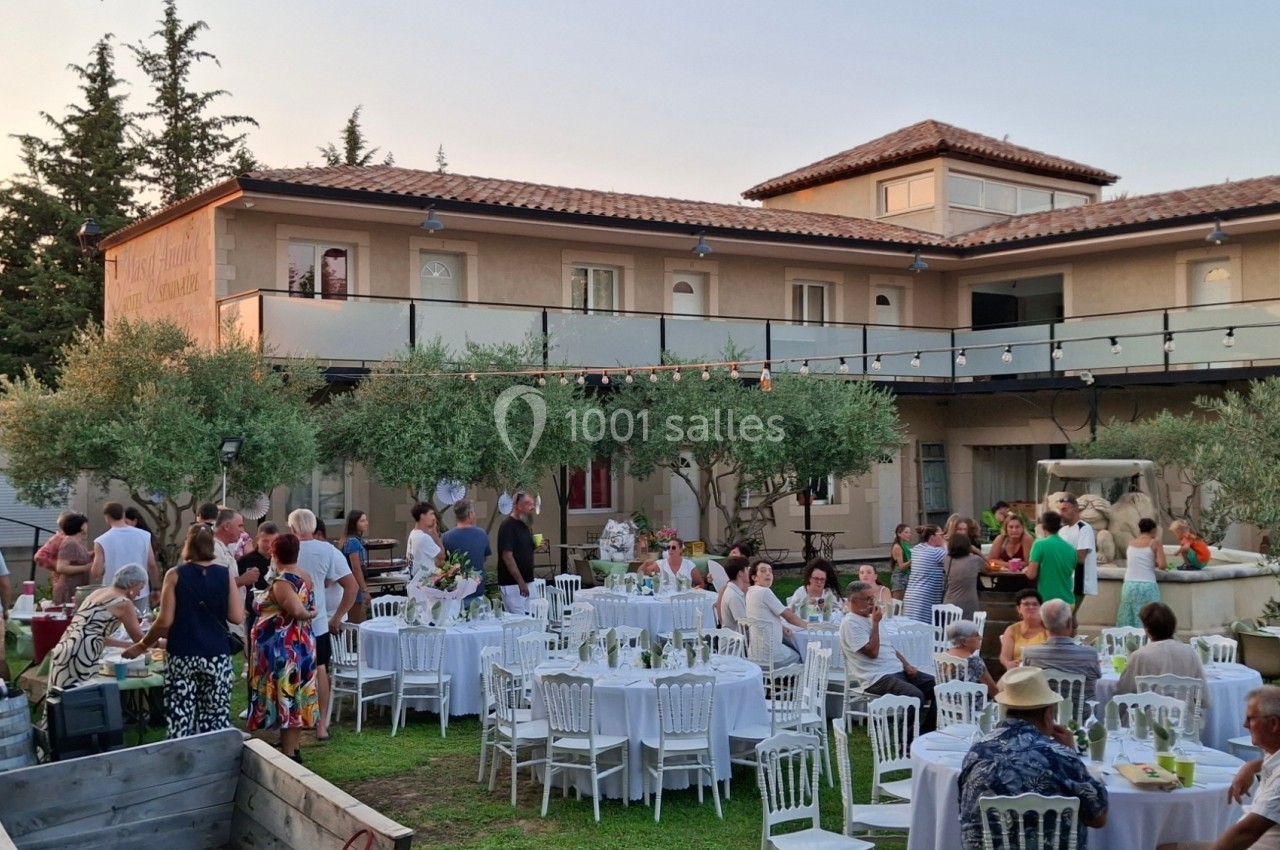 Groupe de personnes réunies dans un jardin avec tables dressées, devant une grande maison au crépuscule.
