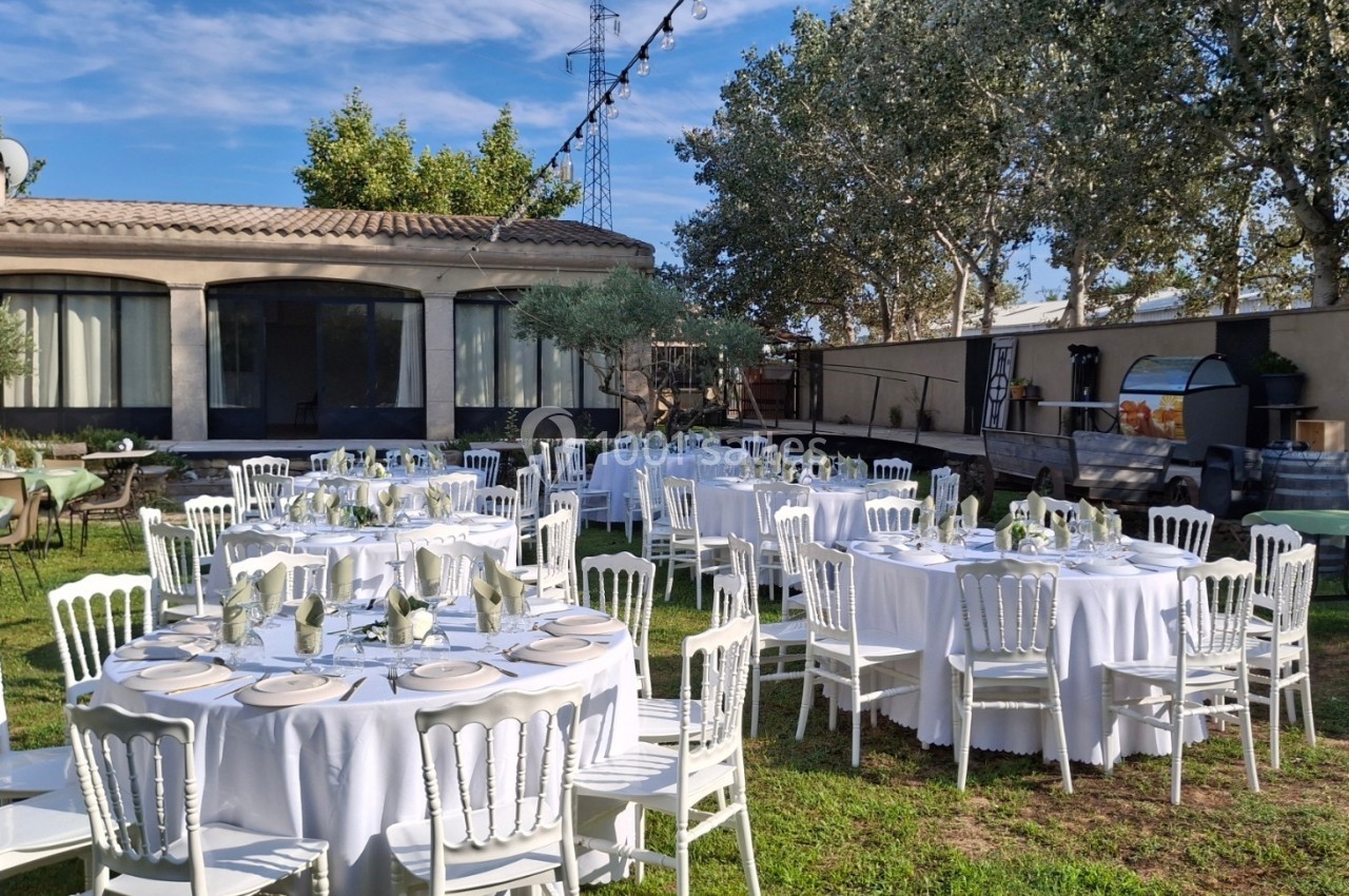 Tables rondes dressées avec nappes blanches et chaises, disposées dans un jardin pour un événement en plein air.