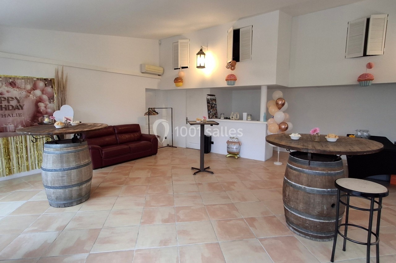 Salle décorée pour un anniversaire avec ballons, guirlande dorée, tonneaux en tables et canapé en arrière-plan.