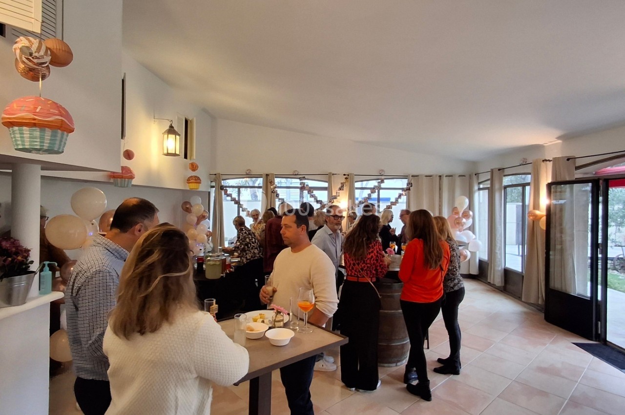 Personnes discutant et partageant un repas dans une salle lumineuse décorée avec des ballons et des suspensions festives.