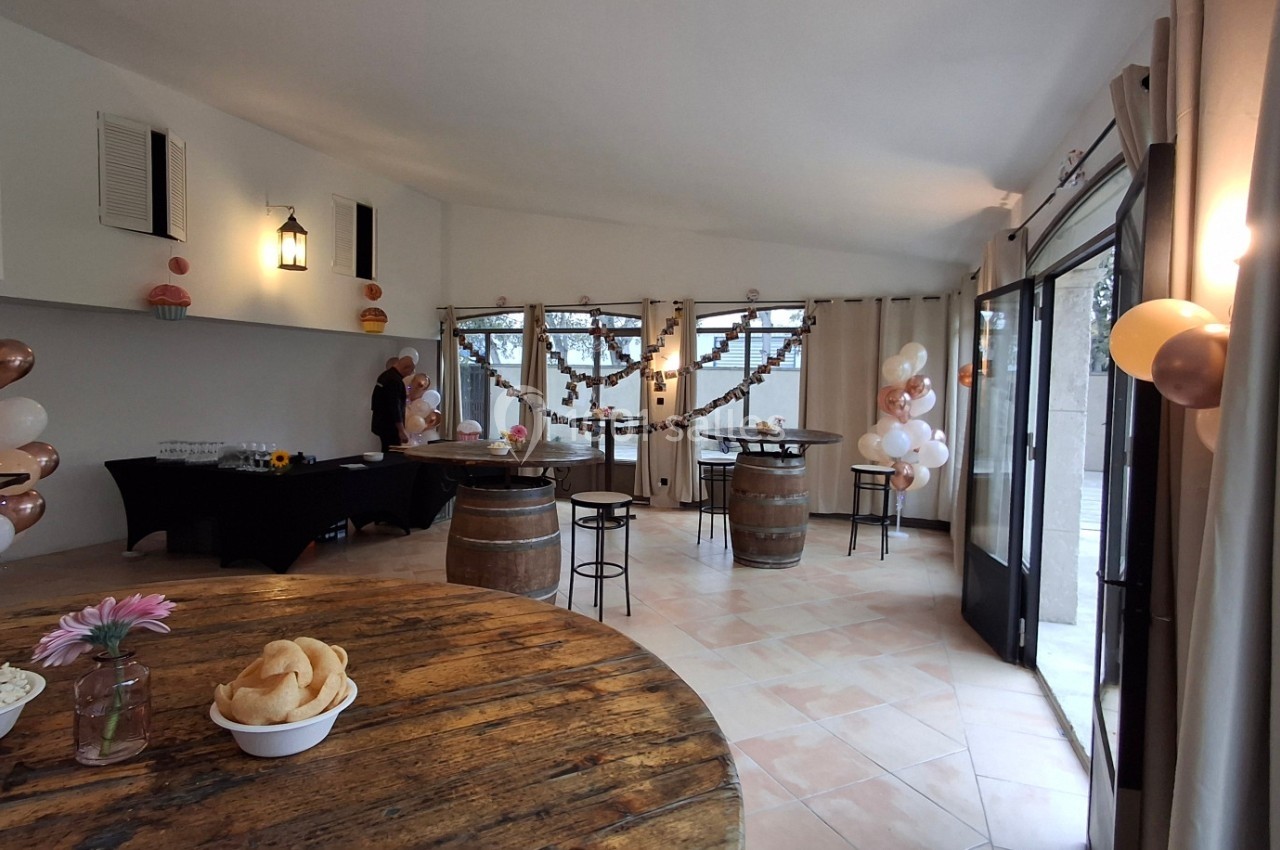 Salle décorée pour un événement avec tables en bois, ballons, guirlandes et buffet dans un espace lumineux.