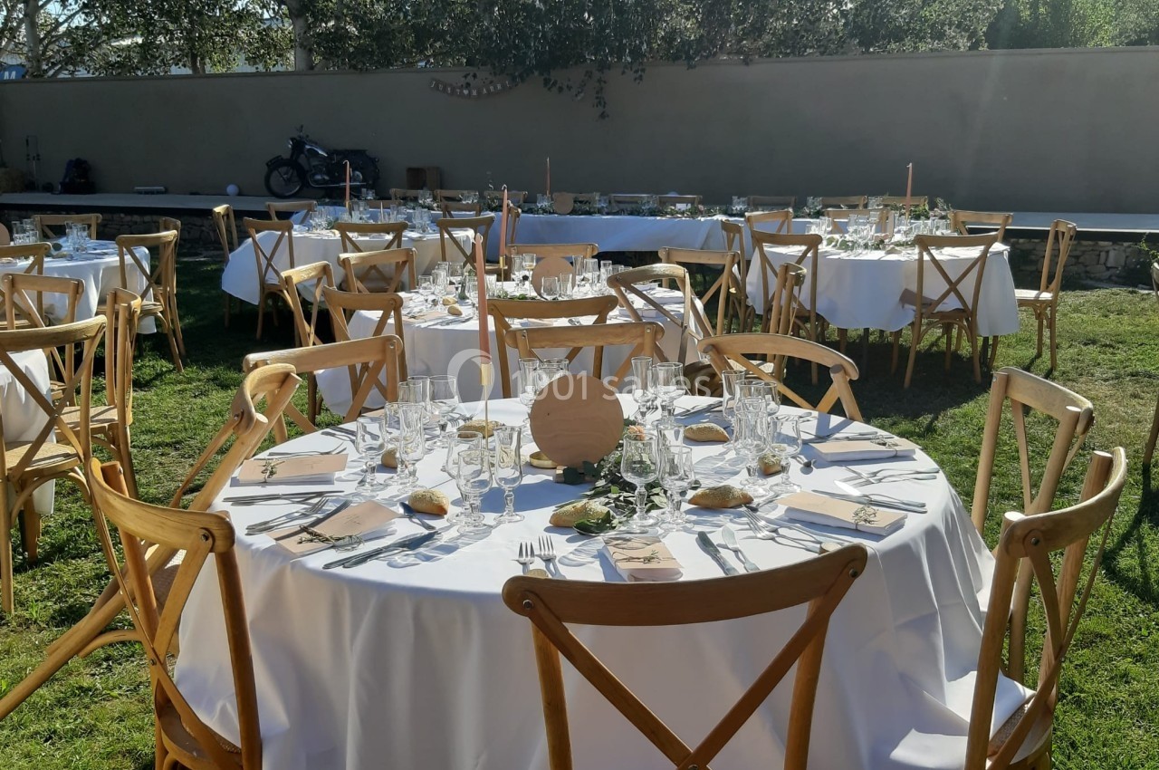 Tables rondes dressées en extérieur avec nappes blanches, chaises en bois et décorations simples pour un événement.