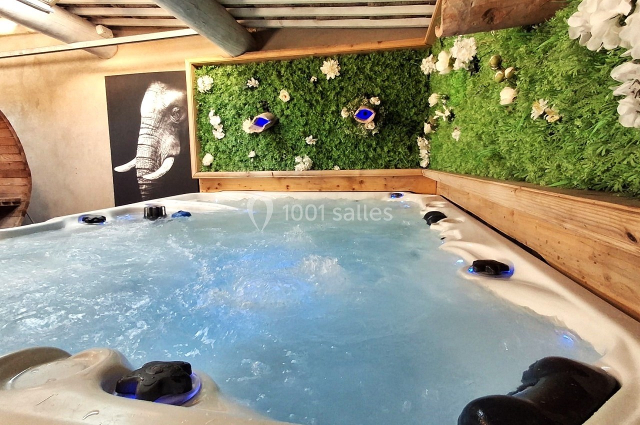 Bain à remous avec eau bouillonnante, encadré de murs en bois et d'un mur végétal décoré de fleurs blanches.