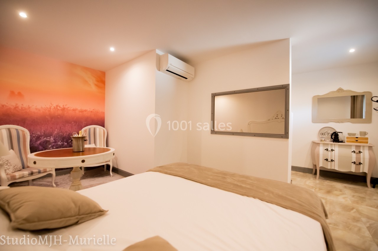 Chambre lumineuse avec lit double, coin salon, mur décoré d'un paysage, climatisation et mobilier classique.