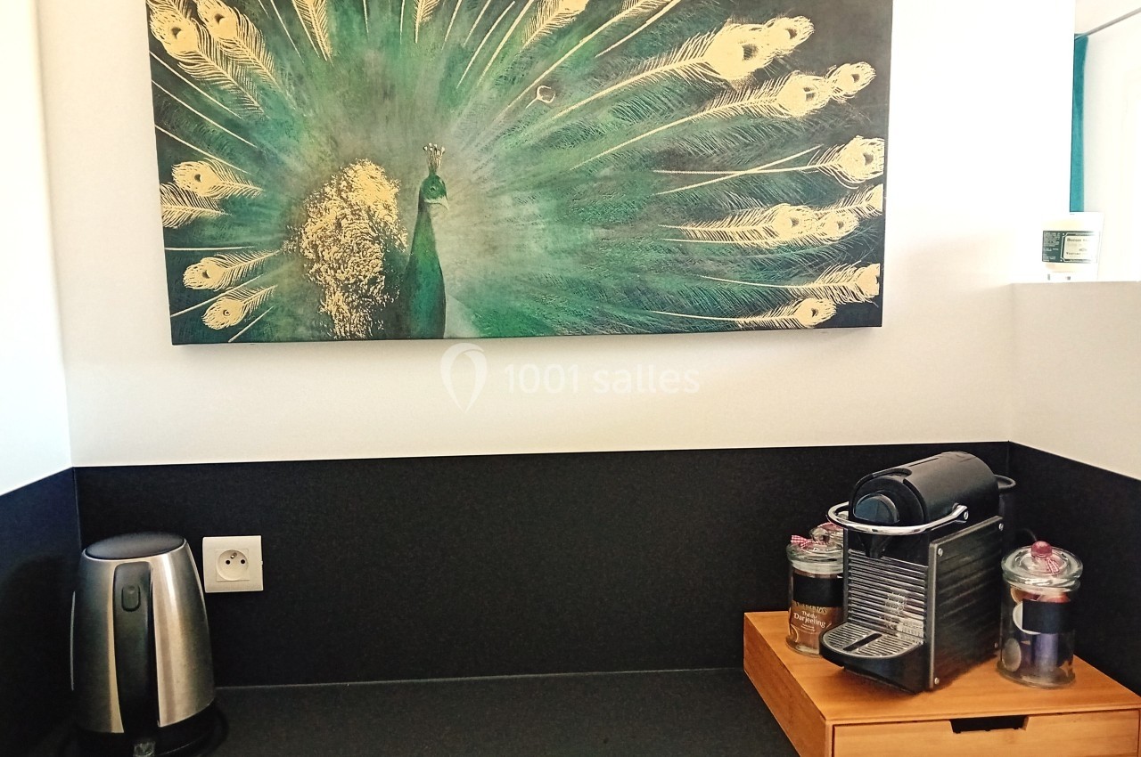 Tableau de paon au plumage déployé accroché au-dessus d'un plan de travail avec une bouilloire et une machine à café.