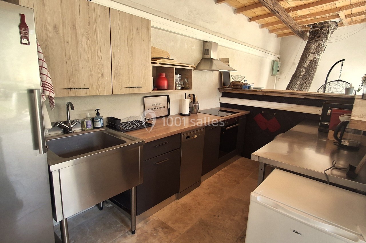 Cuisine moderne avec plan de travail en bois, évier en inox, électroménagers intégrés et plafond en bois apparent.